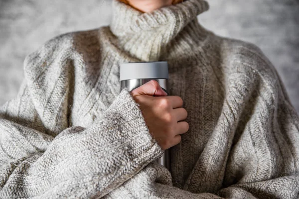 セーターの女性は灰色の壁の背景に熱い飲み物で体温計を持っています — ストック写真