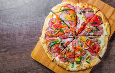 Mozzarella peynirli, jambonlu, domatesli, salamlı, soğanlı, biberli, baharatlı. İtalyan pizzası ahşap masada. 