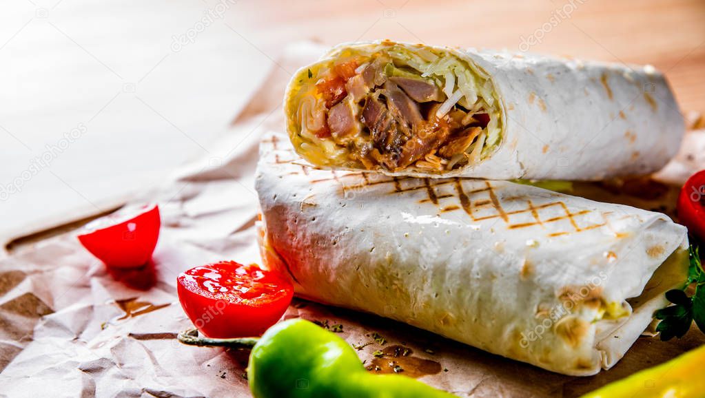 Shawarma with meat and vegetables lies on wooden table background