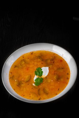 Salatalık turşulu çorba ve beyaz tabakta inci arpa siyah ahşap masa zemininde