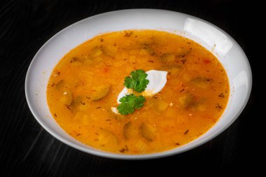 Salatalık turşulu çorba ve beyaz tabakta inci arpa siyah ahşap masa zemininde