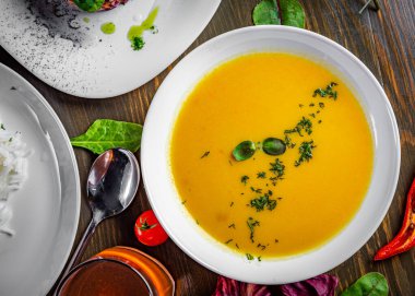 Ahşap masa arkasında beyaz tabakta balkabağı çorbası