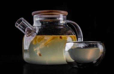 Çay demliği ve bir fincan zencefil çayı. Siyah arka planda bal ve limon.