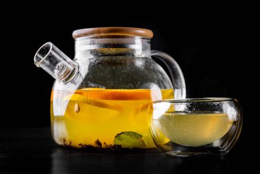 çay demliği ve bir fincan sıcak meyve çayı limon, nane, portakal ve siyah arka plan