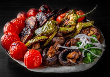 Siyah ahşap masa arkasında tabakta çeşitli sebzeler.