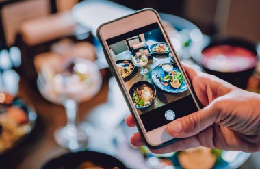 Kadın eli akıllı telefon ile restoranda ya da kafede yemek fotoğrafı çekiyor.
