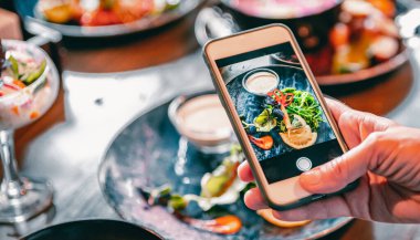 Kadın eli akıllı telefon ile restoranda ya da kafede yemek fotoğrafı çekiyor.