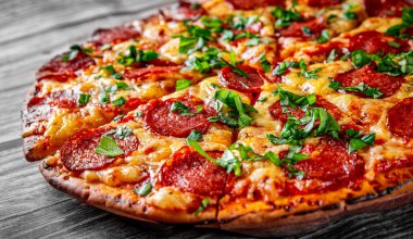 Mozzarella peynirli biberli pizza, salam, domates sosu, biber, baharat ve taze fesleğen. İtalyan pizzası ahşap masa arkasında