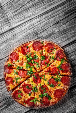 Mozzarella peynirli biberli pizza, salam, domates sosu, biber, baharat ve taze fesleğen. İtalyan pizzası ahşap masa arkasında