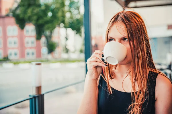 若いですティーンRedhead女の子とともに長い髪とともに熱いコーヒーのカップで街のストリートカフェテラス — ストック写真