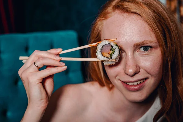 portrait of woman holding chopsticks with sushi in cafe