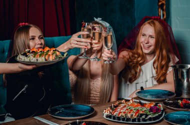 Bir kafede oturup suşi yiyen ve şarap içen üç genç kadın.