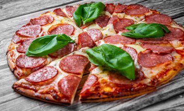 Mozzarella peynirli biberli pizza, salam, domates sosu, biber, baharat ve taze fesleğen. İtalyan pizzası ahşap masa arkasında