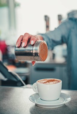 Kahveci kadın kahve kapuçinosunun üzerine tarçın serper ya da kafe 'deki barın tezgahında latte.