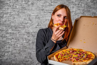 Gri duvar arkasında pizza kutusuyla uzun saçlı esmer bir kızın portresi.