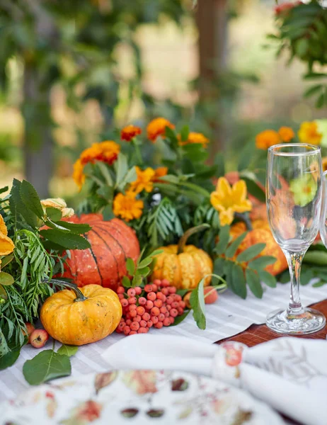 Table setting on a rustic farmhouse country table with white and orange mini pumpkins, and crystal glasses for Thanksgiving Day or Halloween.