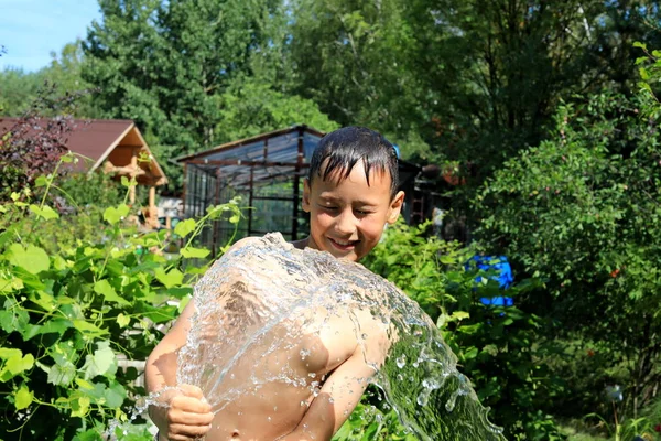 Der Junge mit Spritzwasser an einem sehr heißen Sommertag im Freien — Stockfoto