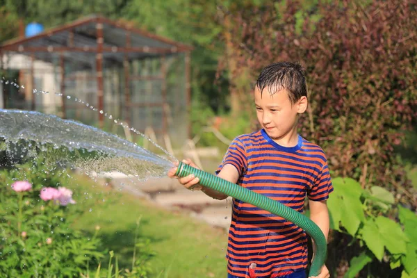 Der Junge mit Spritzwasser an einem sehr heißen Sommertag im Freien — Stockfoto