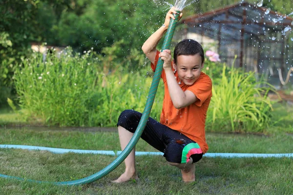 El chico con agua salpicada en un día de verano muy caluroso al aire libre —  Fotos de Stock