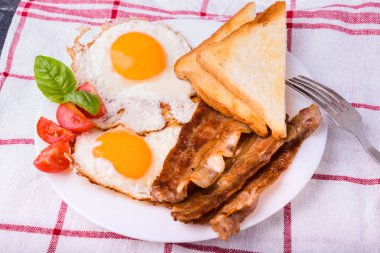 Pastırma ve kızarmış yumurta kahvaltı. Gevrek tost dilim dilimlenmiş kiraz domates, fesleğen yaprakları ile beyaz tabakta servis.