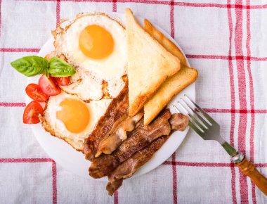Pastırma ve kızarmış yumurta kahvaltı. Gevrek tost dilim dilimlenmiş kiraz domates, fesleğen yaprakları ile beyaz tabakta servis. Üstten görünüm, yukarıdan görünüm.
