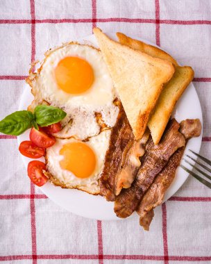 Pastırma ve kızarmış yumurta kahvaltı. Gevrek tost dilim dilimlenmiş kiraz domates, fesleğen yaprakları ile beyaz tabakta servis.