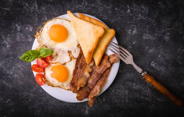 Pastırma ve kızarmış yumurta kahvaltı. Gevrek tost dilim dilimlenmiş kiraz domates, fesleğen yaprakları ile beyaz tabakta servis. Karanlık grunge beton tablo arka plan. Üstten görünüm, yukarıdan görünüm.