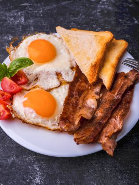 Pastırma ve kızarmış yumurta kahvaltı. Gevrek tost dilim dilimlenmiş kiraz domates, fesleğen yaprakları ile beyaz tabakta servis. Karanlık grunge beton tablo arka planı.