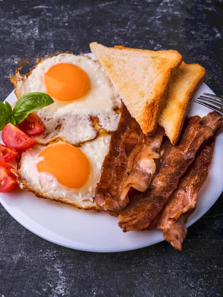 Pastırma ve kızarmış yumurta kahvaltı. Gevrek tost dilim dilimlenmiş kiraz domates, fesleğen yaprakları ile beyaz tabakta servis. Karanlık grunge beton tablo arka planı.