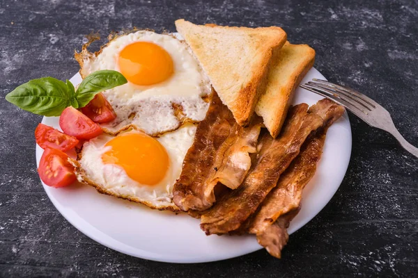 Pastırma ve kızarmış yumurta kahvaltı. Gevrek tost dilim dilimlenmiş kiraz domates, fesleğen yaprakları ile beyaz tabakta servis. Karanlık grunge beton tablo arka planı.