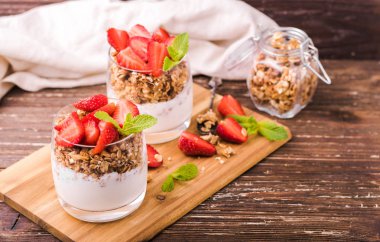 Gözlük granola, çilek ve nane yaprakları ile yoğurt parfait. Ahşap gemide. Sağlıklı kahvaltı kavramı. Rustik ahşap masa arka plan.