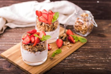 Gözlük granola, çilek ve nane yaprakları ile yoğurt parfait. Ahşap gemide. Sağlıklı kahvaltı kavramı. Rustik ahşap masa arka plan.
