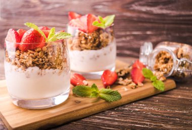 Gözlük granola, çilek ve nane yaprakları ile yoğurt parfait. Ahşap gemide. Sağlıklı kahvaltı kavramı. Rustik ahşap masa arka plan.