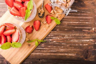 Gözlük granola, çilek ve nane yaprakları ile yoğurt parfait. Ahşap gemide. Sağlıklı kahvaltı kavramı. Rustik ahşap masa arka plan.