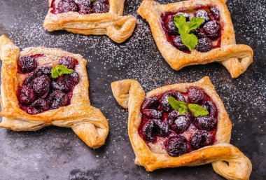 Kiraz ile ev yapımı puf böreği. Tatlı lezzetli tatlı. Nane yaprakları ile süslenmiş. Eski siyah sac pişirme.