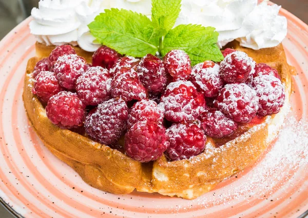 Taze ahududu ve badem pul ile krem şanti ile lezzetli Belçika Waffle. Nane yaprakları ile süslenmiş ve pudra şekeri, turuncu plaka üzerinde. Lezzetli yaz kahvaltı ya da tatlı.