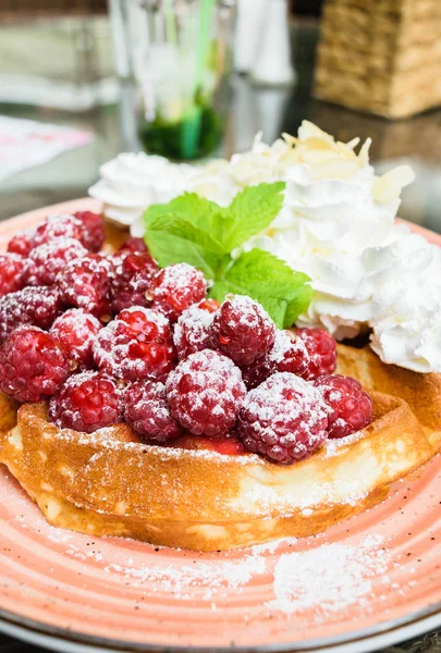 Taze ahududu ve badem pul ile krem şanti ile lezzetli Belçika Waffle. Nane yaprakları ile süslenmiş ve pudra şekeri, turuncu plaka üzerinde. Lezzetli yaz kahvaltı ya da tatlı.