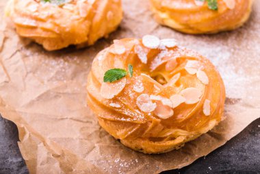 Ev yapımı choux pasta kek Paris Brest badem pul ve pudra şekeri ile. Smallmint yaprakları ile süslenmiş. Parşömen kağıt üzerine. Fırın kavramı