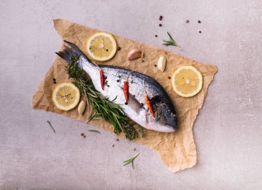 Taze dorado balık. Dorado ve pişirme malzemeleri - biberiye, baharat, limon, sarımsak, kekik, otlar. Pişirme kavramı. Taş ışık arka plan üzerinde. üstten görünüm, yukarıdan görünüm.