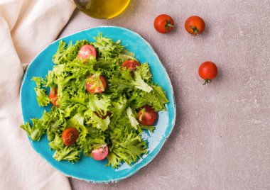 Frisee ve mavi seramik plaka üzerinde domates salatası. Sağlıklı gıda kavramı. En iyi görünümü yukarıdaki. Taş masa lambası arka plan.