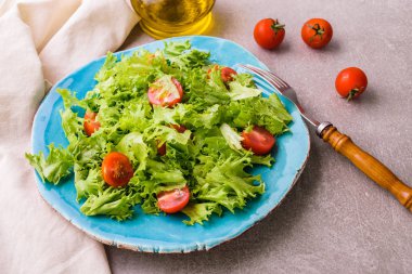 Frisee ve mavi seramik plaka üzerinde domates salatası. Sağlıklı gıda kavramı. En iyi görünümü yukarıdaki. Taş masa lambası arka plan.