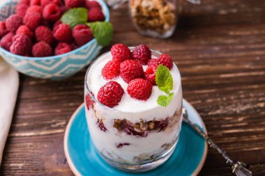 Katmanlı yoğurt granola ve ahududu. Bir bardakta, nane yaprakları ile süslenmiş. Karanlık rustik ahşap masa arka plan üzerinde. Sağlıklı gıda kavramı.