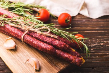 Kabanosy - geleneksel Lehçe domuz sosisi ahşap kesme tahtası üzerinde füme. Biberiye bitki, diş sarımsak ve domates ile. Rustik ahşap tablo