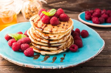 Ahududu ve çikolata şurubu, nane yaprakları ile süslenmiş ile Amerikan krep yığılmış. Ahşap rustik masa zemin üzerine mavi tabakta servis.