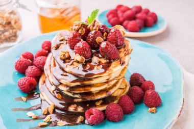 Ahududu ve çikolata şurubu, granola ile serpilir ve nane yaprakları ile süslenmiş ile Amerikan krep yığılmış. Taş masa lambası arka plan mavi tabakta servis. 