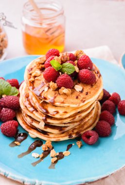Ahududu ve çikolata şurubu, granola ile serpilir ve nane yaprakları ile süslenmiş ile Amerikan krep yığılmış. Taş masa lambası arka plan mavi tabakta servis. 
