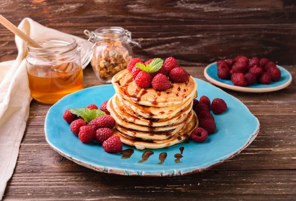 Ahududu ve çikolata şurubu, nane yaprakları ile süslenmiş ile Amerikan krep yığılmış. Ahşap rustik masa zemin üzerine mavi tabakta servis.