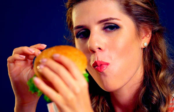 Dziewczyna otworzyła usta, trzymając hamburger na wyciągniętej ręce i zamknęła oczy. — Zdjęcie stockowe