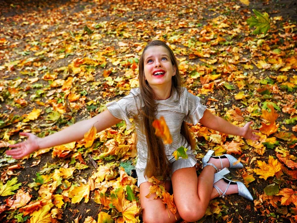 Autumn fashion dress child girl sitting fall leaves park outdoor.