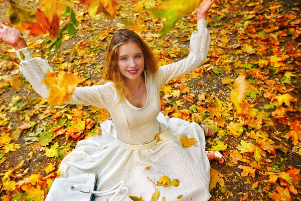 Autumn fashion dress woman sitting fall leaves city park outdoor.